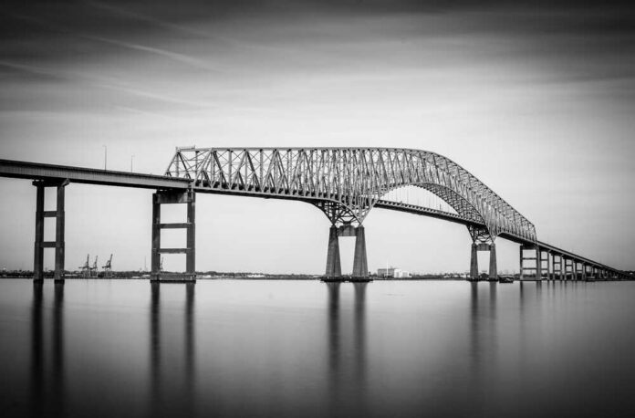 A large bridge spanning over a calm body of water in black and white