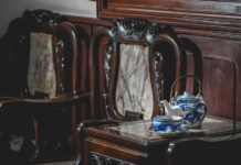 A wooden table with a blue and white teapot and cup next to ornate wooden chairs