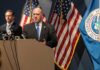 Tech Giants Comply—Unmasking Dissenters for DHS! Government officials speaking at a press conference with U.S. flags in the background