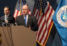 Tech Giants Comply—Unmasking Dissenters for DHS! Government officials speaking at a press conference with U.S. flags in the background