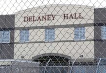 Prisoner in orange jumpsuit sits on bunk in jail cell