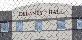 Prisoner in orange jumpsuit sits on bunk in jail cell