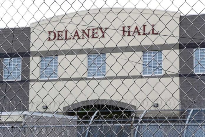 Prisoner in orange jumpsuit sits on bunk in jail cell