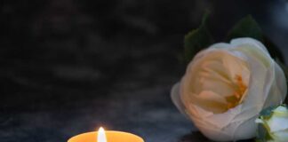 A lit candle beside a white flower on a dark surface