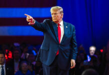 Person in suit pointing on stage with audience watching