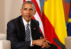 Unpaid Millions Haunt Obama Showcase Man in a dark suit seated with flags in the background