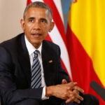 Unpaid Millions Haunt Obama Showcase Man in a dark suit seated with flags in the background