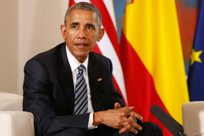 barack-obama1376446241jpg Man in a dark suit seated with flags in the background