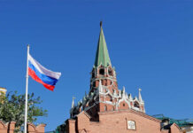 Russian flag and Kremlin tower against a clear blue sky
