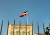 Wall Street Cheers, Tehran Cashes In? Iranian flag waving above a government building against a blue sky