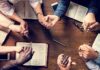 Group holding hands around open books on a wooden table