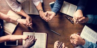 Group holding hands around open books on a wooden table