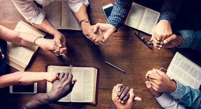 Group holding hands around open books on a wooden table