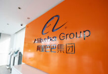 Code Ban Twist: Alibaba Flips The Script Alibaba Group logo on an orange wall in a modern office lobby