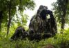 camouflaged soldiers observing through binoculars in a forest