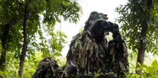 camouflaged soldiers observing through binoculars in a forest