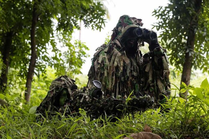 camouflaged soldiers observing through binoculars in a forest