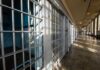 Budget Sledgehammer Slams Trans Care Interior view of a prison corridor with jail cells and sunlight streaming through windows