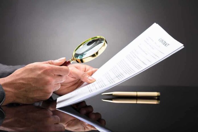 Hands holding magnifying glass over contract document