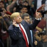 man in suit gestures with raised finger at a crowded event