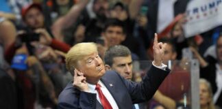 man in suit gestures with raised finger at a crowded event