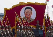 Military parade featuring soldiers and a large banner of Kim Il-sung