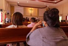 people seated in church pews facing a cross