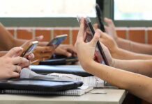 students' hands using smartphones at a classroom table