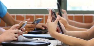 students' hands using smartphones at a classroom table