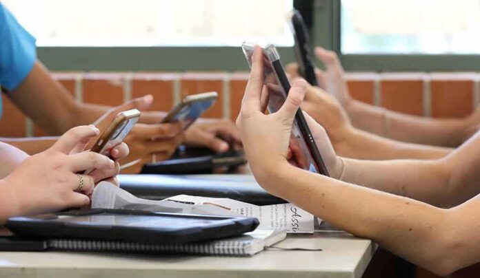 students' hands using smartphones at a classroom table
