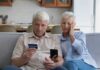Seniors Blindsided: 22% Cut Ahead Older couple on couch looking at credit card and phone