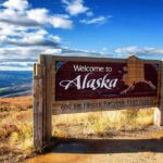 wooden welcome sign with Alaska map by open landscape