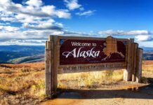 wooden welcome sign with Alaska map by open landscape