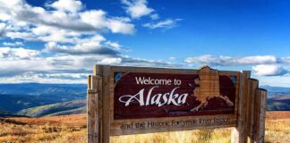 wooden welcome sign with Alaska map by open landscape