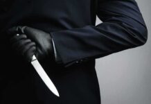 Person in dark suit holding a knife behind their back
