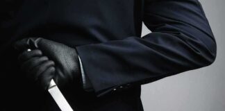 Person in dark suit holding a knife behind their back