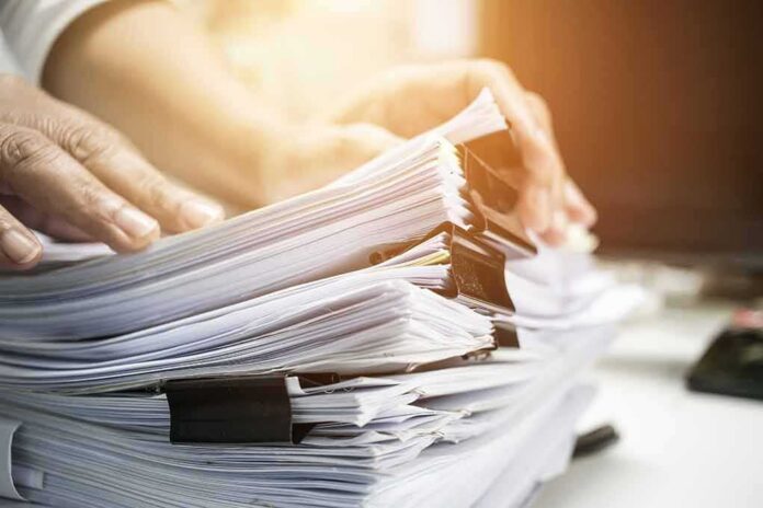 shutterstock_692559100 Hands sorting a large stack of paper documents with binder clips