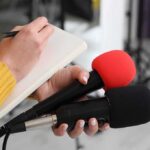 VP’s Baby Upends Beltway Norms Journalist holding two microphones while writing in a notebook
