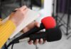 Journalist holding two microphones while writing in a notebook