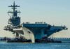 Rust-Streaked Carrier Hides Grimmer Story Aircraft carrier guided by tugboats in a harbor