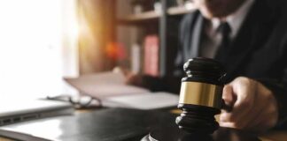 Judge's gavel on desk with person reading documents in background