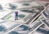 Miniature businessman standing on US dollar bills