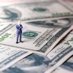 Miniature businessman standing on US dollar bills