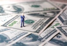 Trump Slashes $810M – Constitutional Brawl Erupts Miniature businessman standing on US dollar bills