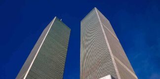 Twin rectangular skyscrapers rising above a hotel facade against a clear blue sky