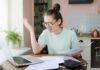 Bank Report: Parents Bankroll Grown Kids Young woman with glasses frustrated at laptop while holding bills