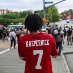 Person in red football jersey films a street protest