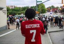 Person in red football jersey films a street protest
