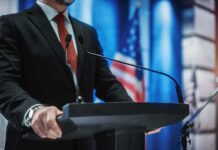 man in suit at podium with microphones