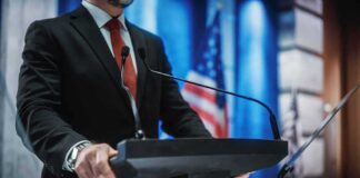 man in suit at podium with microphones
